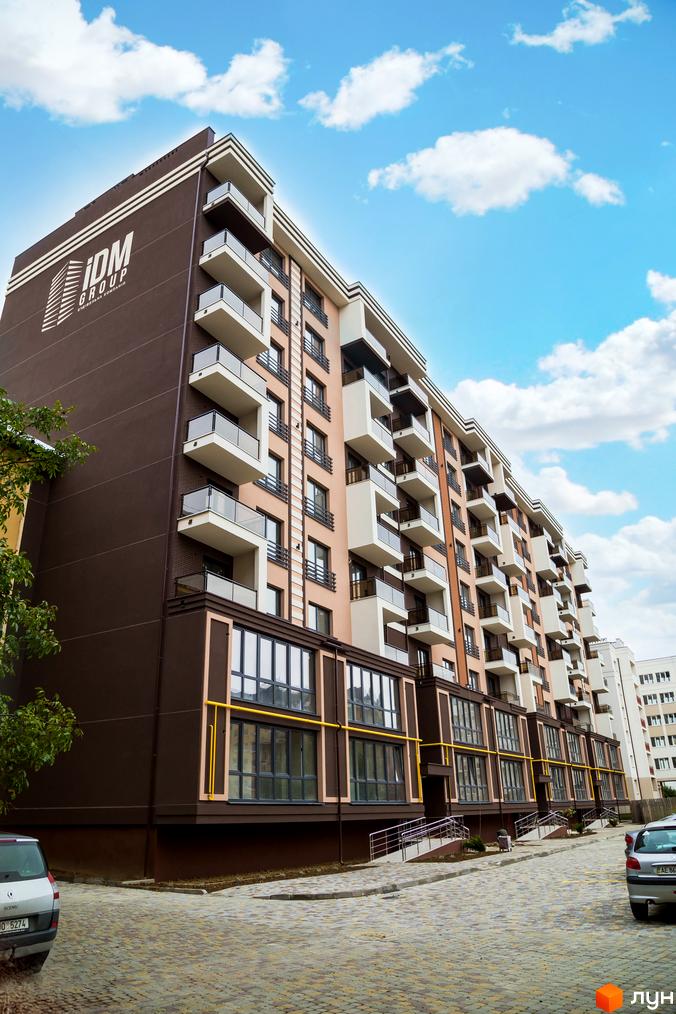 Багатоповерховий будинок Житлового комплексу Modern коричневого та світлого кольорів з балконами. Прибудинкова територія вимощена бруківкою, є зелені насадження та парковка.