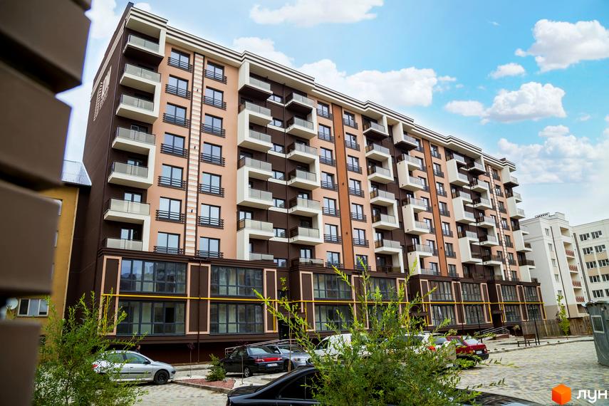 Житловий комплекс Modern: багатоповерховий будинок коричневого та світло-бежевого кольорів з балконами. На прибудинковій території розташовані автомобілі та зелені насадження.