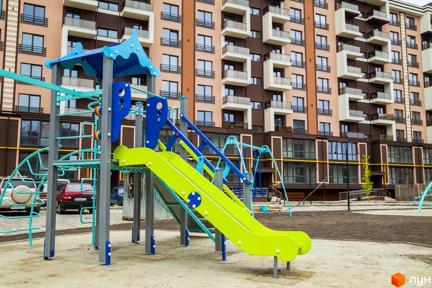 Житловий комплекс Modern, будинок з світло- та темно-коричневими фасадами та балконами. На прибудинковій території облаштований дитячий майданчик з гіркою та гойдалками.