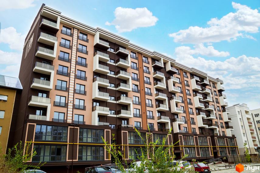 Новобудова Modern: багатоповерхова будівля з бежево-коричневим фасадом, балконами зі скляними поручнями. Навколо зелені насадження та парковка.