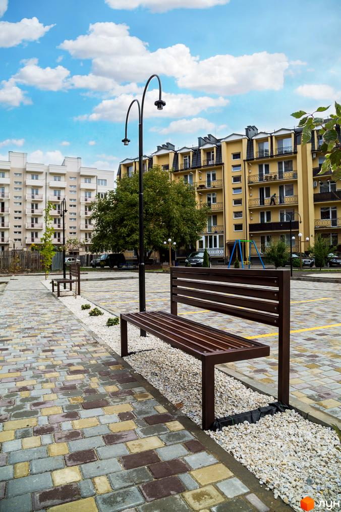 Зображення фасаду та прибудинкової території Житлового комплексу Modern. На передньому плані лавка та ліхтар, позаду – будівлі.