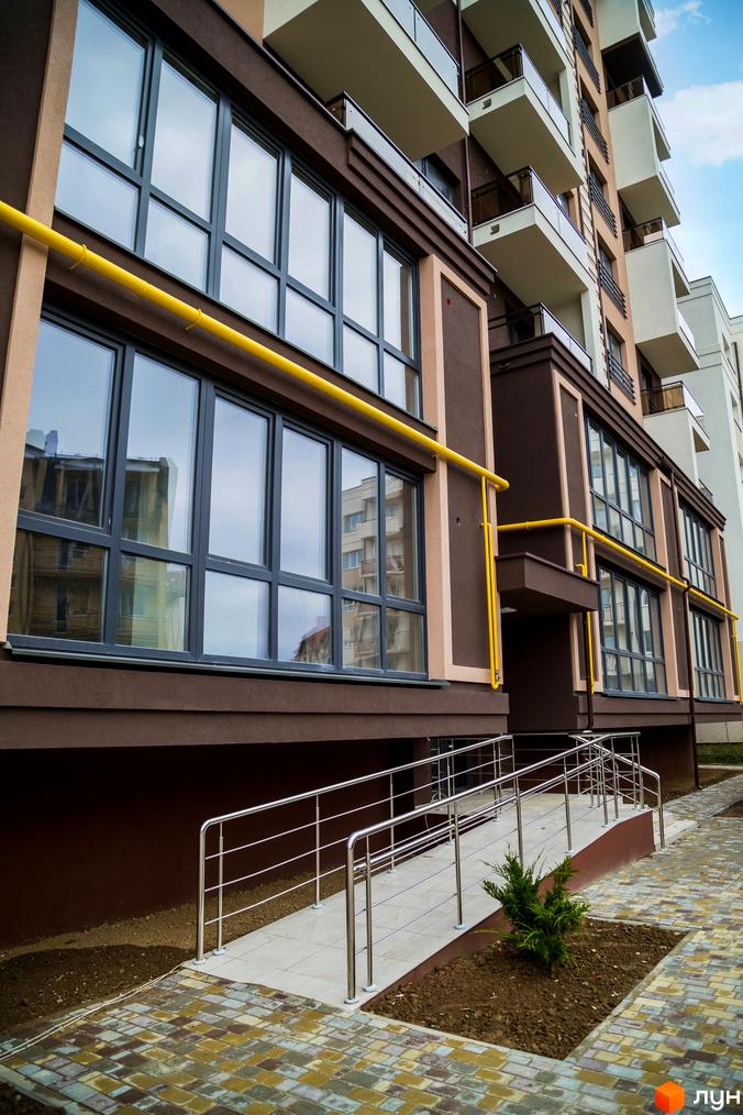 Зовнішній вигляд будинку в Житловому комплексі Modern. Фасад будинку з великими вікнами та жовтими газовими трубами, біля будинку облаштований тротуар.