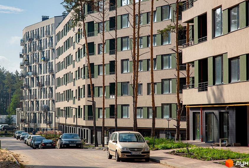 Житловий комплекс Park Town з фасадами пісочного кольору та зеленими віконницями. На передньому плані дорога з припаркованими автомобілями.