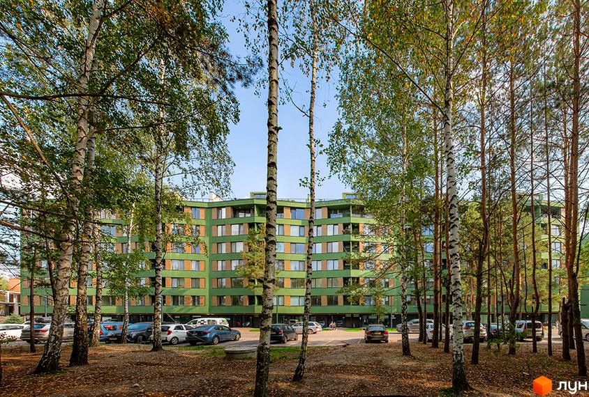 Зелений багатоповерховий будинок ЖК Park Town з великими вікнами. На передньому плані дерева, а на території парковка для автомобілів.