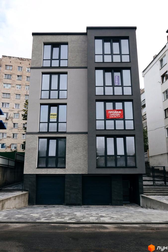 Клубний будинок „Над Ставом“: фасади з сірої цегли та штукатурки, великі вікна, гаражні ворота. Поруч сусідні будинки, бруківка.