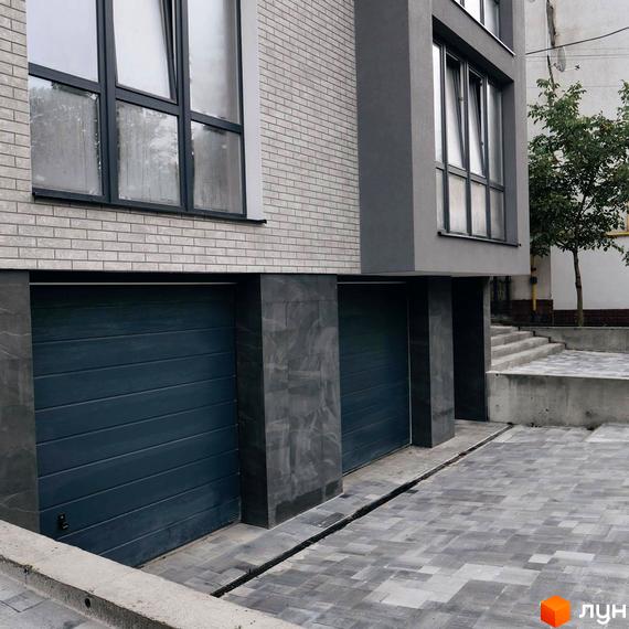 Клубний будинок Над Ставом: фасади з цегляною кладкою та темними елементами, два гаражні ворота та вимощена бруківкою територія.