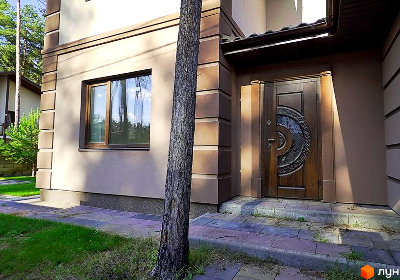 Котеджне містечко КМ Сонячний 2. Фасад будинку з вікном та вхідними дверима, поруч дерево та доріжка з плитки.