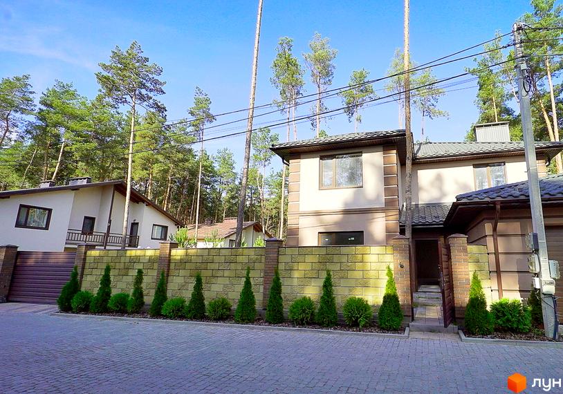 Котеджне містечко Сонячний 2: фасад будинку з цегляним оздобленням та вікнами, огороджений цегляним парканом з туями та кущами.