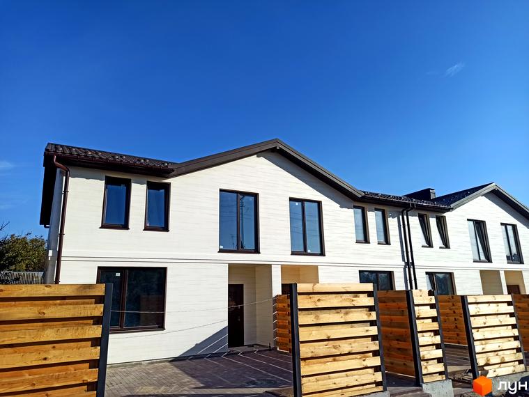 Фасад Таунхаусів Travertino: білі будинки з коричневими дахами та темними вікнами. На передньому плані видно дерев'яну огорожу.