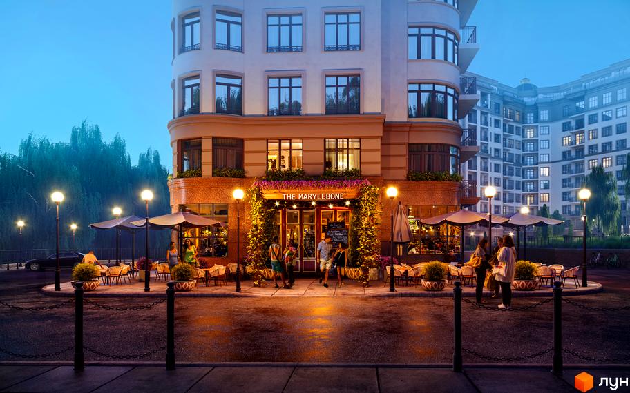 Житловий комплекс The Marylebone з терасами та ліхтарями на вулиці. Навколо будівлі столики з парасольками та зелені насадження.