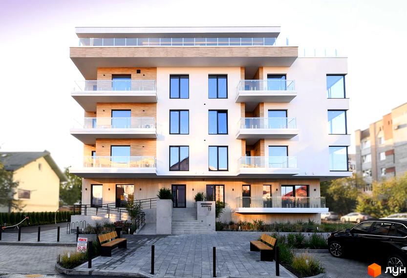 Житловий комплекс Baltiysʹka Hall з білим фасадом, дерев'яними вставками та скляними балконами. Прибудинкова територія облаштована лавками та зеленню.