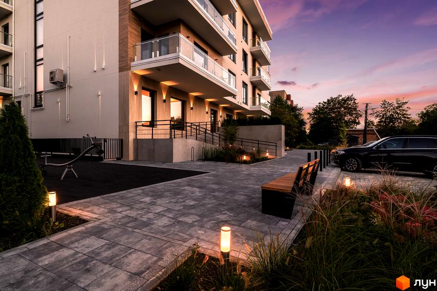 Житловий комплекс Baltiysʹka Hall з багатоповерховим будинком світлих тонів, балконами та підсвіткою фасаду. Прибудинкова територія має мощення, лавки, озеленення та освітлення.