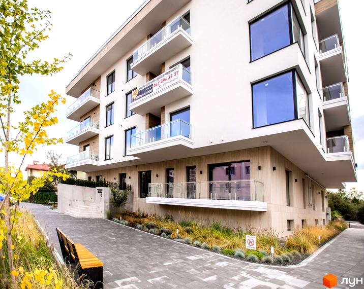 Житловий комплекс Baltiysʹka Hall з білим фасадом, великими вікнами та балконами. Прибудинкова територія з доріжкою, лавкою та осіннім озелененням.