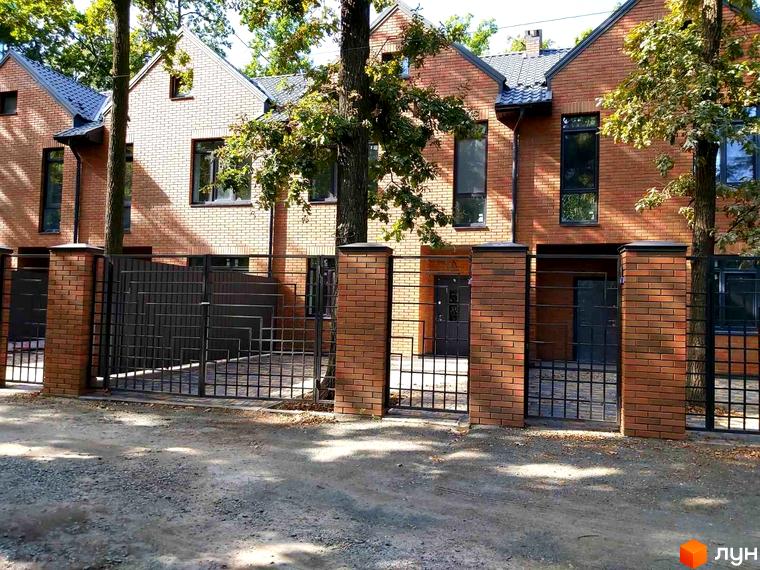 Таунхаус Brighton Lisova – цегляні будинки з чорними вікнами та дверима, огороджені металевою брамою та цегляними колонами. Навколо зелені дерева.