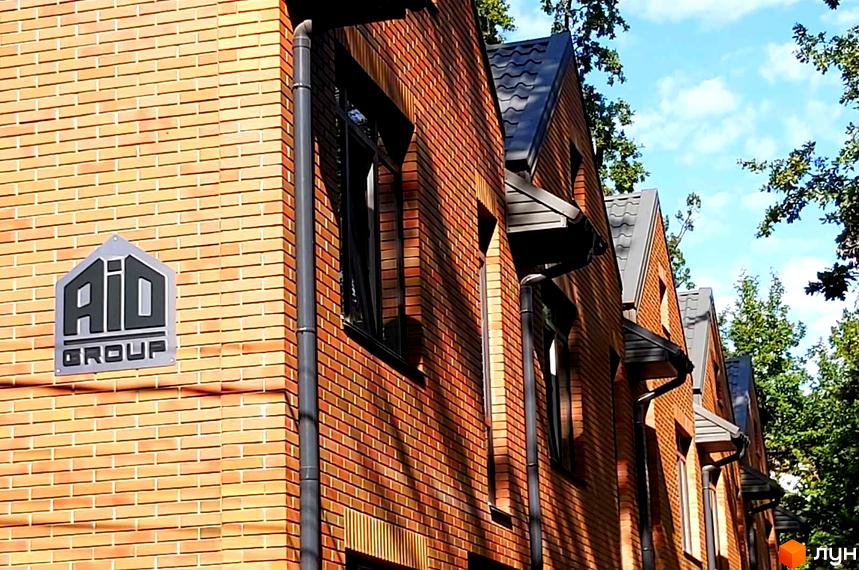 Фасад Комплексу таунхаусів Brighton Lisova з цегляними стінами, темними вікнами та дахом. Навколо видно зелені дерева та синє небо.