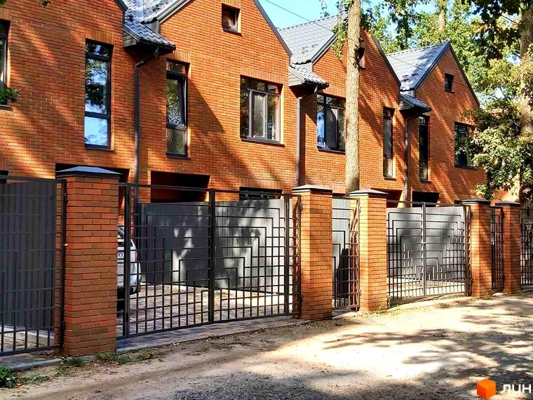 Таунхаус Brighton Lisova: будинки з червоної цегли, сірі дахи та металева огорожа з геометричним візерунком. Перед ними гравійна дорога.