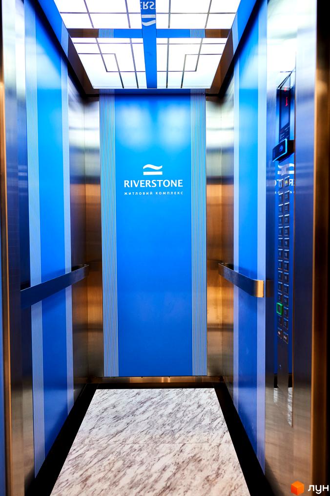 Сучасний ліфт у житловому комплексі RiverStone з синіми стінами та мармуровою підлогою. Внутрішній дизайн створює комфортну атмосферу.