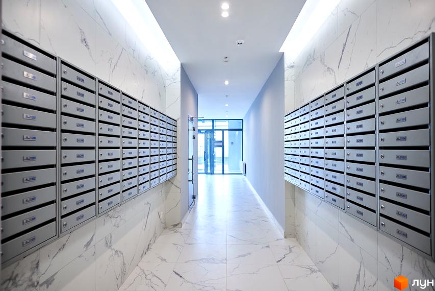 Сучасний вхід у житловий комплекс RiverStone з поштовими скриньками по обидва боки. Просторий коридор з великими вікнами, що забезпечують природне освітлення.