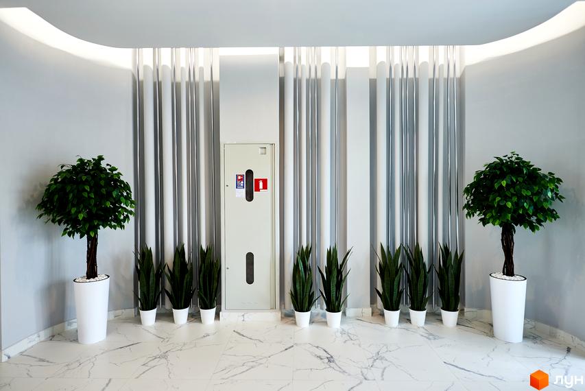 Сучасний інтер'єр житлового комплексу RiverStone з рослинами в горщиках та мармуровою підлогою.