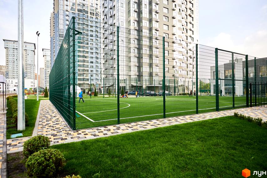 Зовнішній вигляд житлового комплексу RiverStone з футбольним полем та прибудинковою територією з зеленими насадженнями.