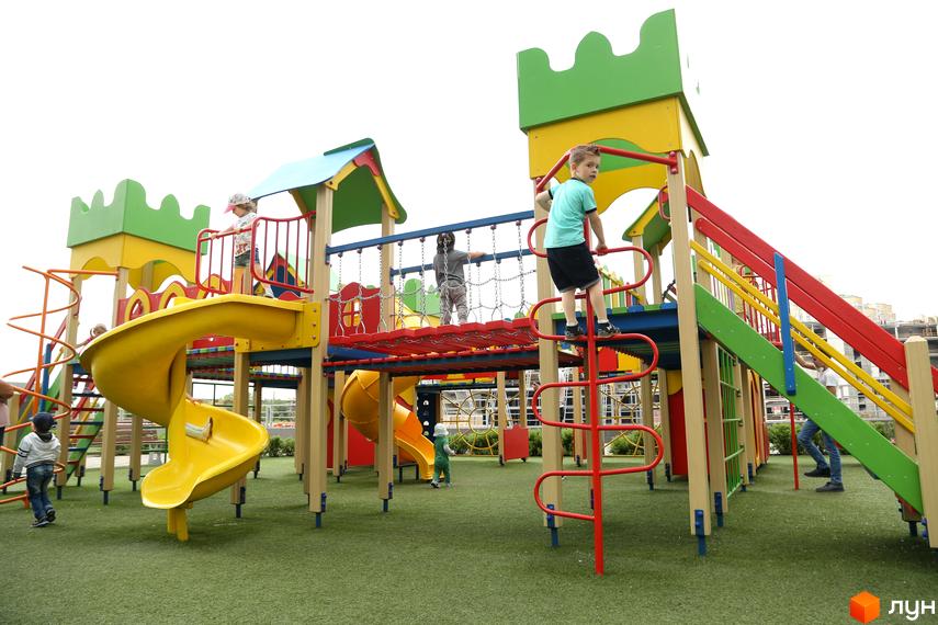 Дитячий майданчик у житловому комплексі RiverStone з яскравими гірками та безпечним покриттям. Діти граються на сучасній ігровій зоні.