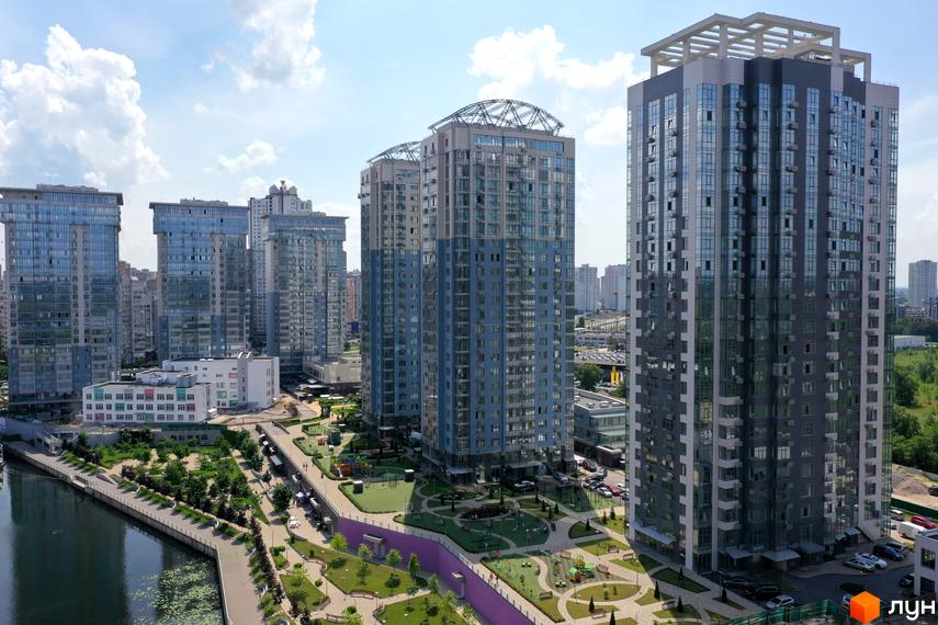 Житловий комплекс RiverStone: висотні будинки з блакитними та сірими фасадами, що стоять біля річки. На прибудинковій території розташовані дитячі майданчики та зелені зони.