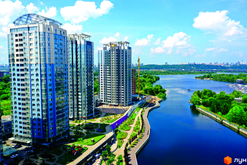 Житловий комплекс RiverStone: висотні будинки з блакитними та сірими фасадами, що виходять на річку. Прибудинкова територія з дитячими майданчиками та зеленими зонами.