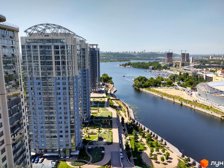 Вид на висотні будинки ЖК RiverStone з видом на річку та міський пейзаж. На території комплексу розташовані зелені зони та дитячі майданчики.
