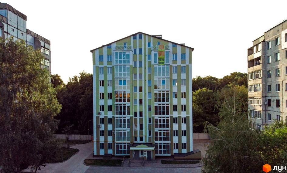 Будинок житлового комплексу на вулиці Гостиннодвірській, 14в, з фасадом у зелено-білу смужку та великою кількістю вікон. Навколо будинку розташовані дерева та доглянута прибудинкова територія.