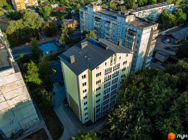 Житловий комплекс на вулиці Гостиннодвірська, 14в, з жовто-білим фасадом та сірим дахом, оточений деревами. Поруч розташовані інші багатоповерхові будинки та дорога.