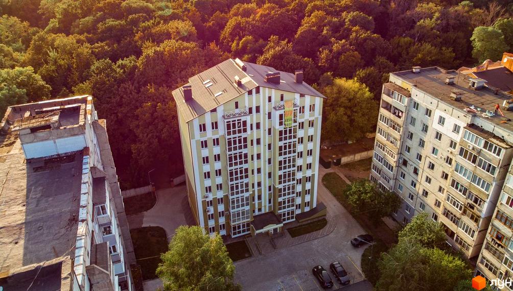 Житловий комплекс на вулиці Гостиннодвірській, 14в, з фасадом у смужку та прибудинковою територією з деревами та парковкою.