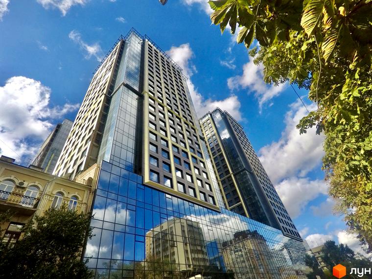 БФК Metropole - сучасний житловий комплекс з високими будівлями та скляними фасадами. Навколо комплексу зелені дерева та блакитне небо з хмарами.