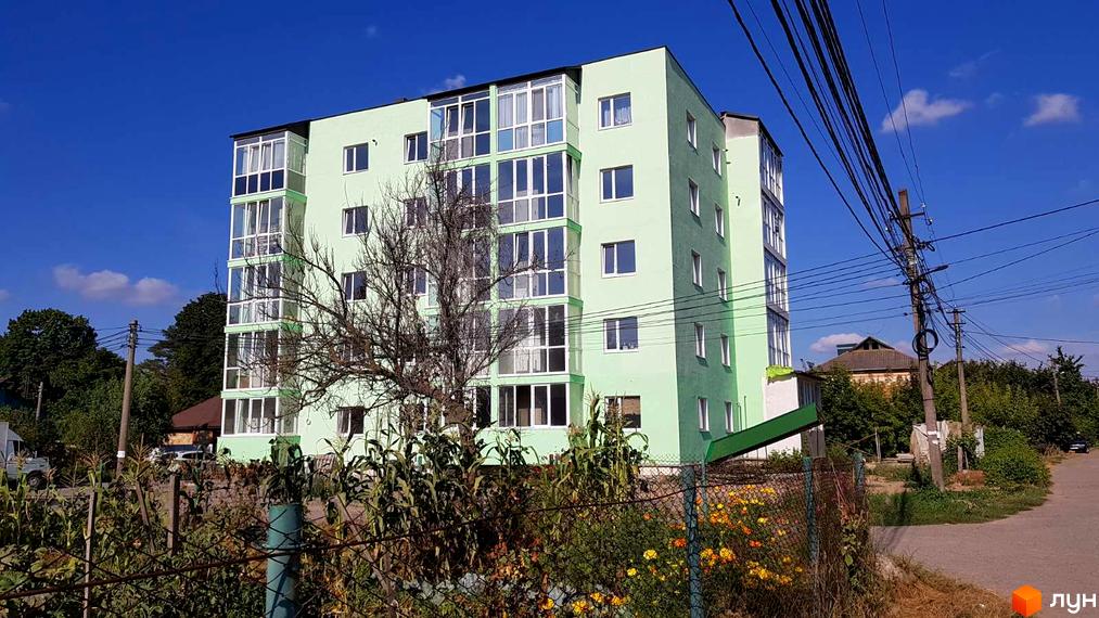 Зображення сторінки житлового комплексу Лайм. Багатоповерховий будинок салатового кольору з великими вікнами. На передньому плані видно дерева та огорожу.