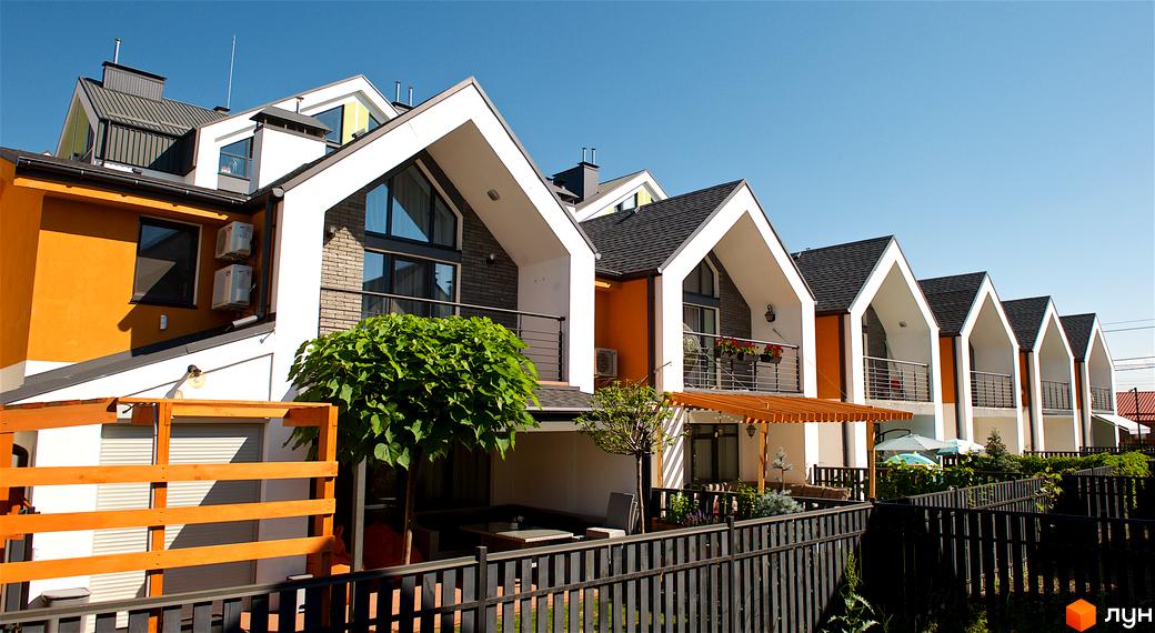 Таунхауси „Петрівське містечко“ – фасади будинків з білими та помаранчевими елементами, темним дахом та балконами. Прибудинкова територія з зеленими насадженнями та парканом.