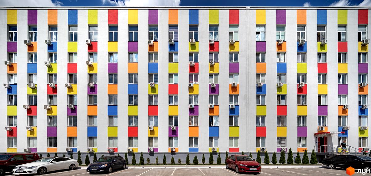 Фасад житлового комплексу Бестужевські сади з яскравими кольоровими смугами та кондиціонерами. Перед будинком розташована парковка з автомобілями.