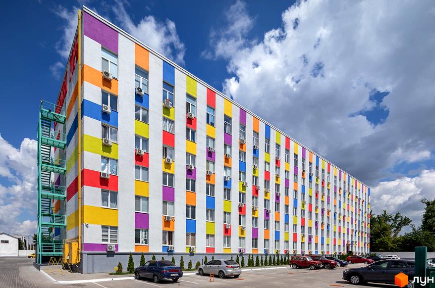 Житловий комплекс Бестужевські сади з яскравим фасадом у смужку та парковкою перед будинком. Зовнішній вигляд новобудови з кондиціонерами на вікнах.