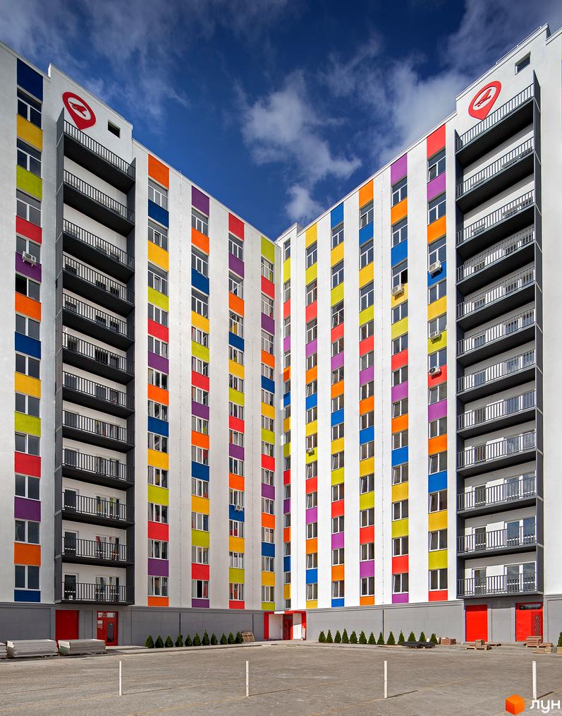 Яскравий фасад будівлі ЖК Воробйові гори з кольоровими смугами. На прибудинковій території розташована парковка та зелені насадження.