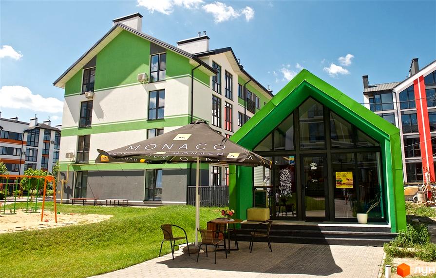 Житловий комплекс Петрівське містечко. Фасад будинку в зелених та білих тонах, поруч кафе та дитячий майданчик.