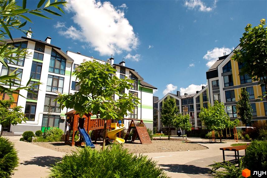 Житловий комплекс Петрівське містечко: фасади будинків з панорамними вікнами та зеленою зоною з дитячим майданчиком. Сучасна архітектура новобудови.