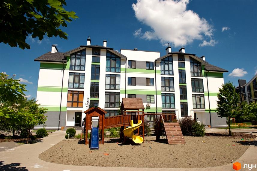 Житловий комплекс Петрівське містечко з фасадом біло-зеленого кольору та дитячим майданчиком. Зовнішній вигляд новобудови та прибудинкова територія.
