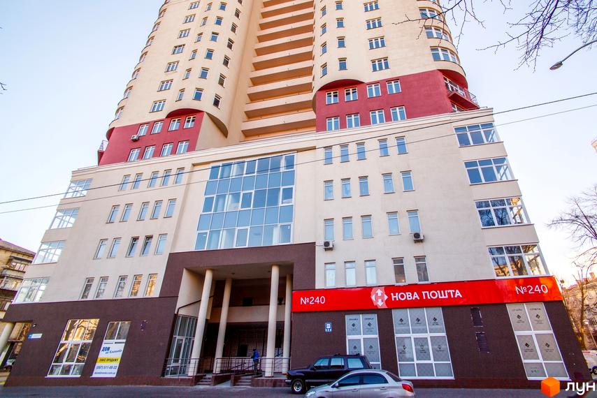 Багатоповерховий будинок Житлового комплексу Будинок на Клименка з бежевим та червоним фасадом, великими вікнами та вхідною групою. На першому поверсі розташоване відділення Нової Пошти.