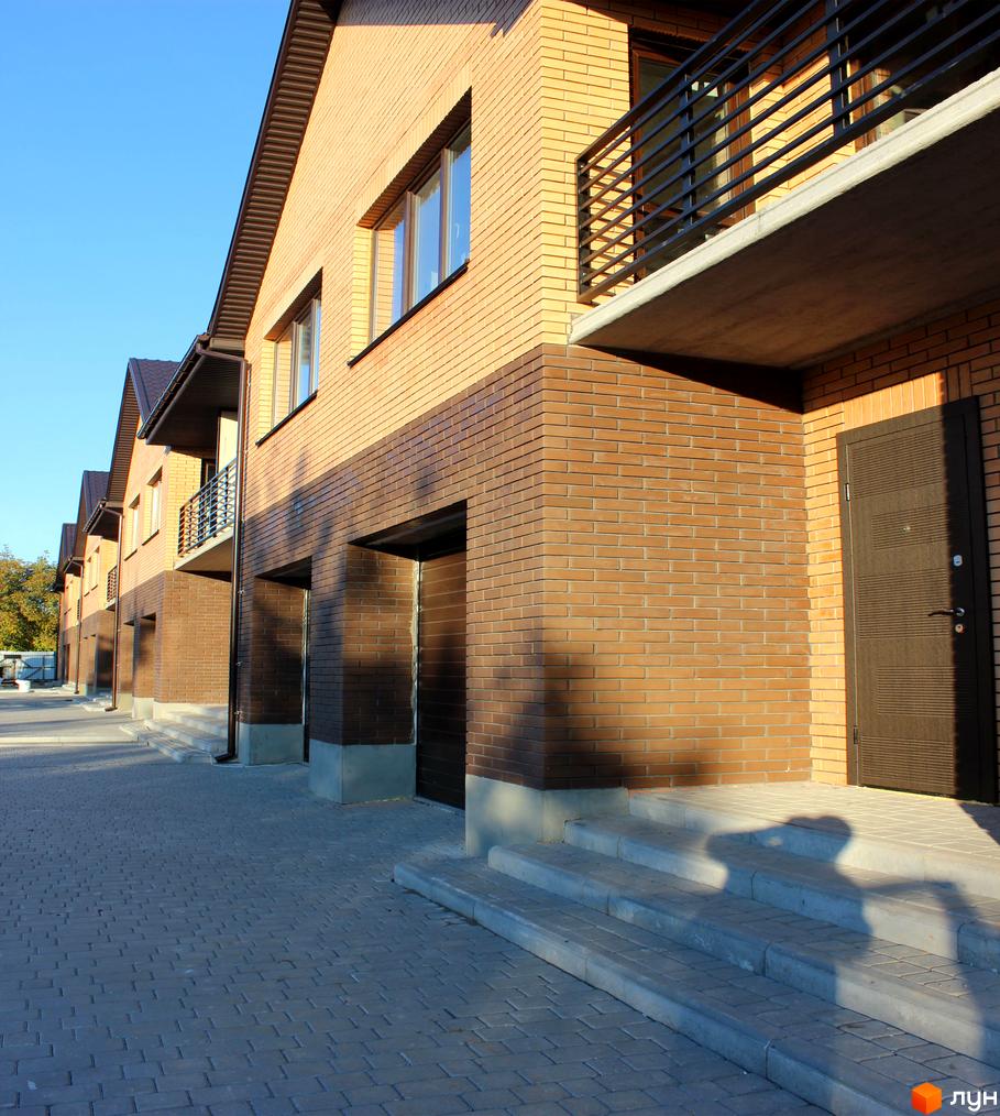 Ряд таунхаусів WestSide з фасадами з цегли світло-коричневого та темно-коричневого кольорів, балконами та вимощеною бруківкою прибудинковою територією.