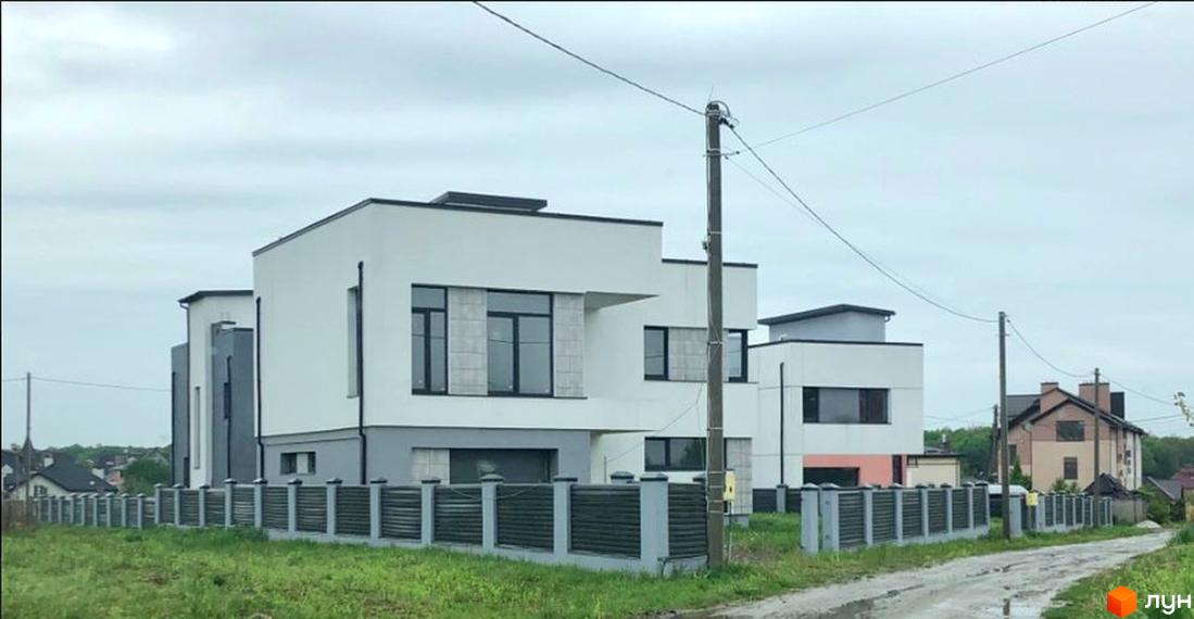 Котеджне містечко OneSide House: білі будинки з плоскими дахами та темними вікнами, оточені огорожею та ґрунтовою дорогою.