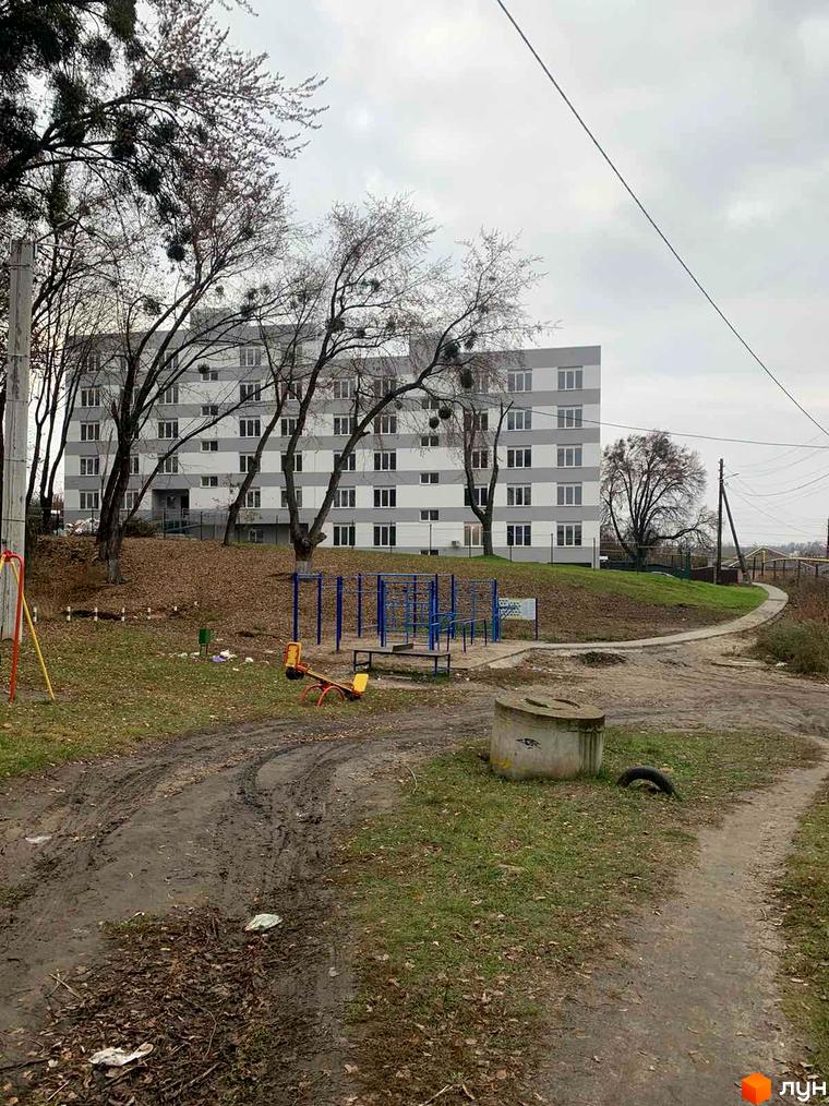 Житловий комплекс Муромець: багатоповерховий будинок з горизонтальними сіро-білими смугами, оточений дитячим майданчиком та осінніми деревами.