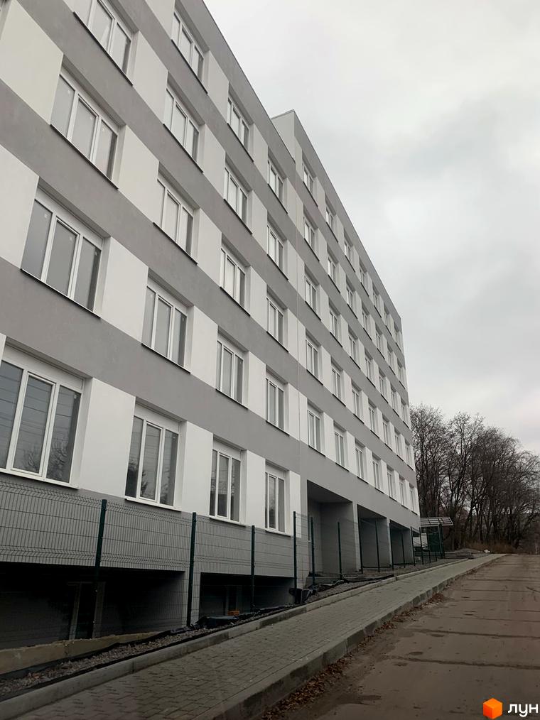 Висока багатоповерхова будівля ЖК Муромець з великими вікнами. Поруч розташована дорога з тротуаром та зелений паркан.