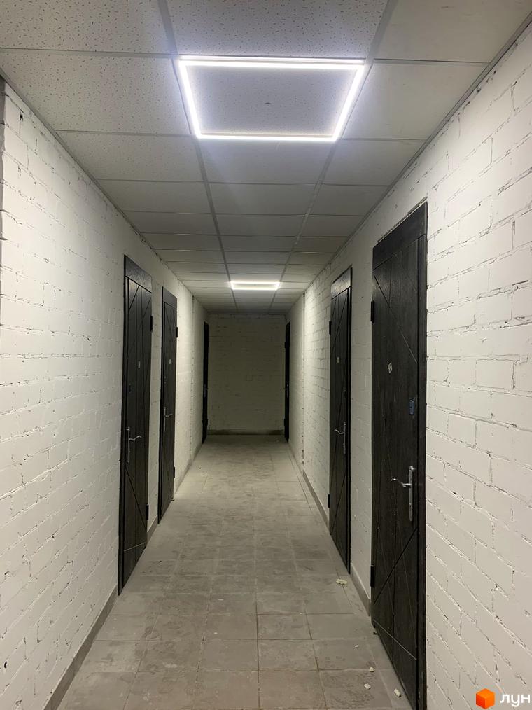 Коридор у будинку ЖК Муромець з білими цегляними стінами та темними дверима, освітлений квадратними світильниками на стелі.