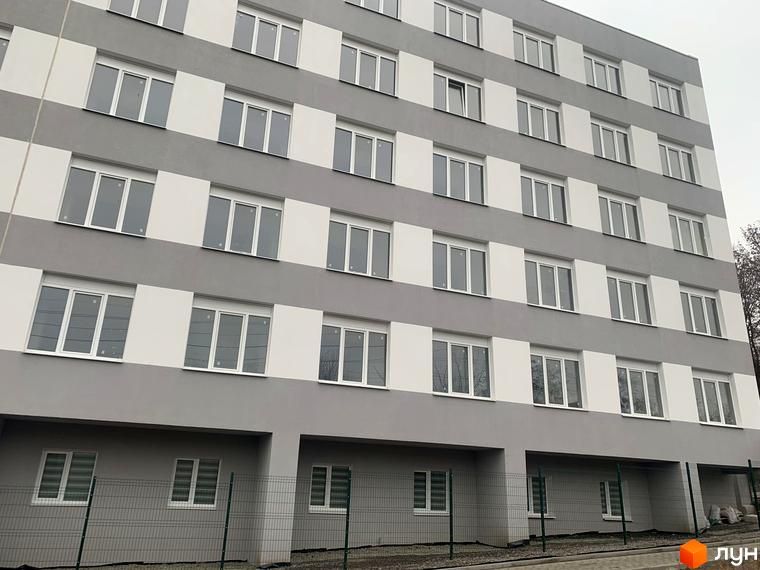 Новобудова Муромець: багатоповерховий житловий будинок у сіро-білих тонах з численними вікнами. На передньому плані видно зелений паркан.