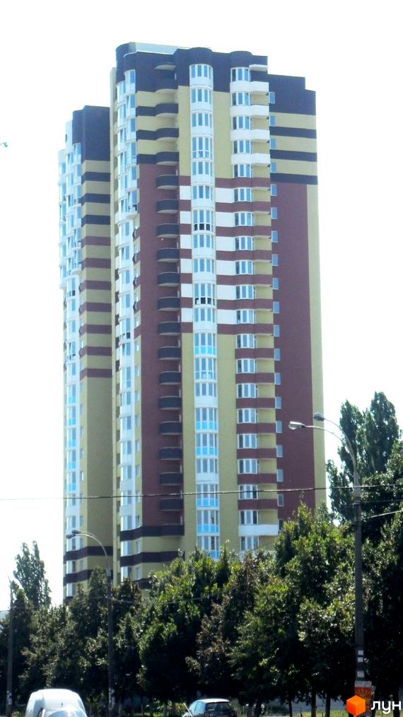 Житловий комплекс на Харківському шосе, 182 – багатоповерхова новобудова з яскравим фасадом, що поєднує жовті, коричневі та бордові секції. Навколо будівлі зелені дерева та міська інфраструктура.