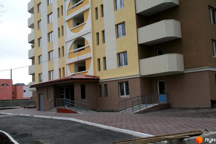 Зовнішній вигляд новобудови на вул. Хорольська, 1а. Будинок має жовто-білий фасад з балконами та прибудинкову територію з бруківкою та пандусами.