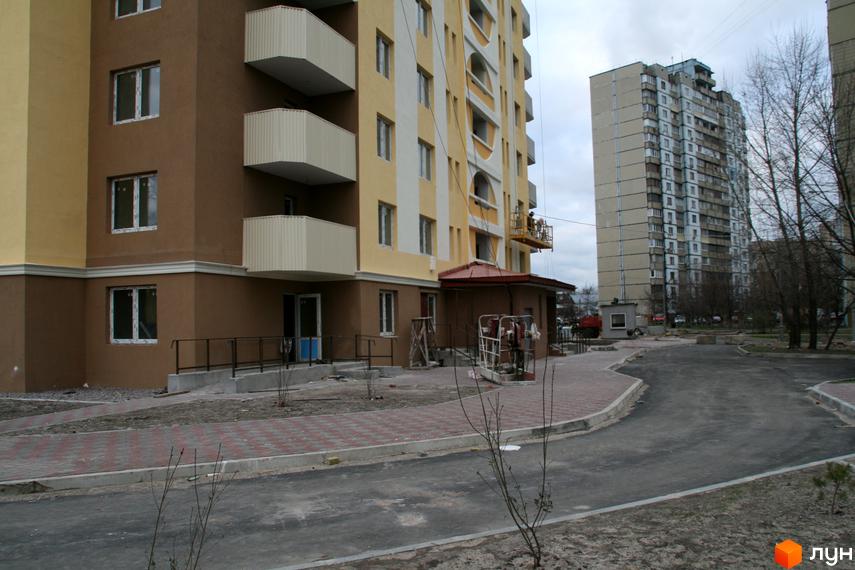 Зовнішній вигляд новобудови на вул. Хорольська, 1а. Будинок має коричнево-жовту облицьовку та балкони. Прибудинкова територія з бруківкою та дорогою.